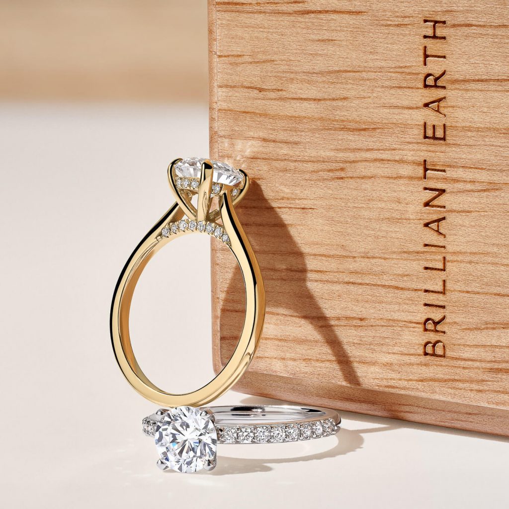 Yellow gold engagement ring and white gold engagement ring resting on Brilliant Earth wooden ring box