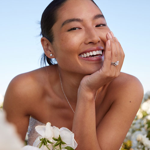 Bride smiles wearing engagement ring and wedding ring in field of white flowers