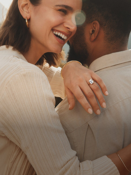 Couple wearing gold diamond engagement ring and assortment of fine jewelry.