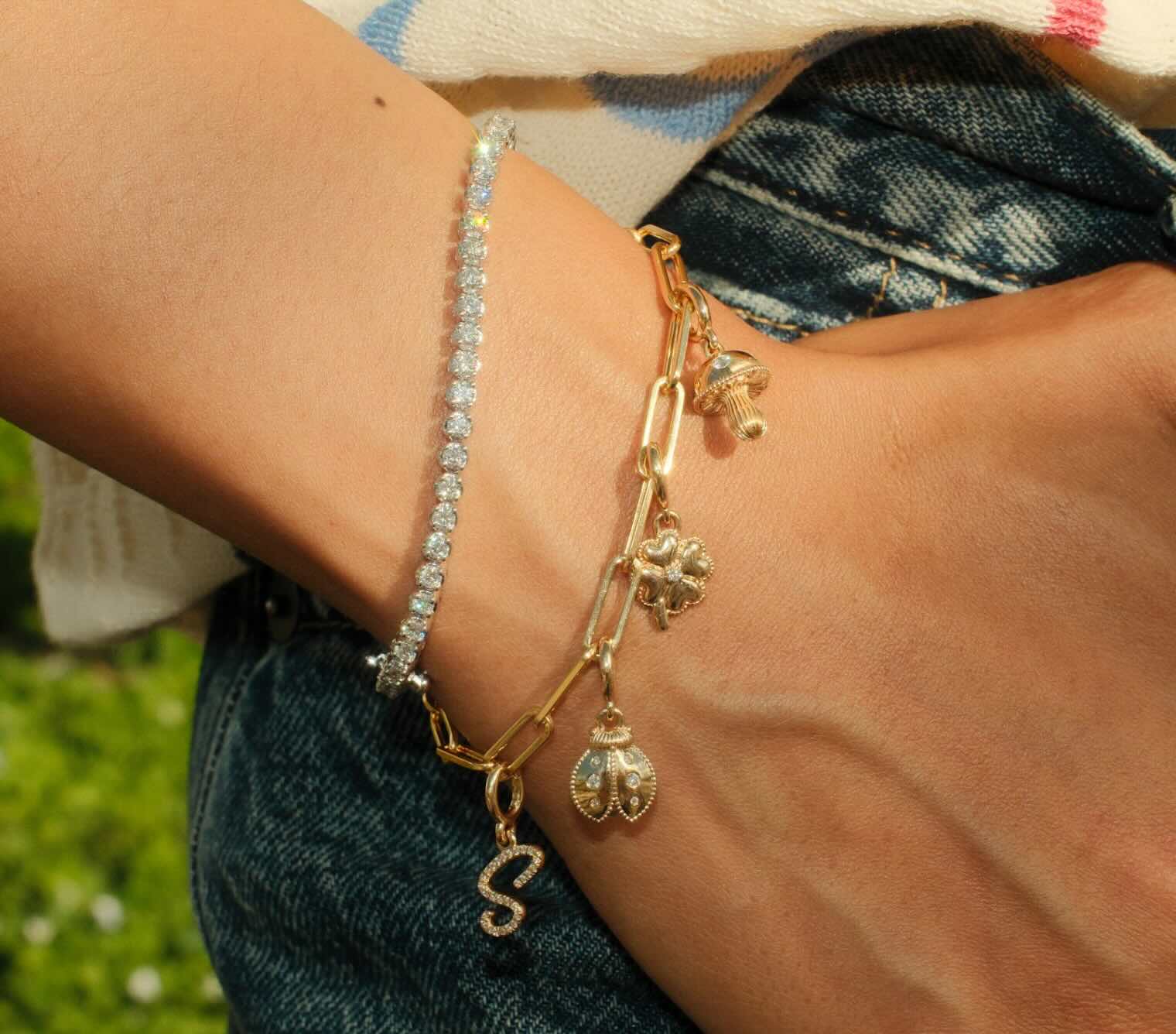 Model wearing a gold charm bracelet and diamond tennis bracelet.